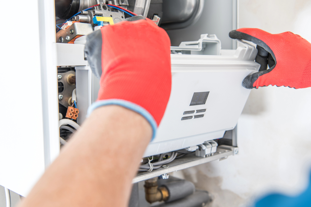 A person wearing red gloves is servicing or repairing the front panel of a boiler or heating system, reflecting the dedication and expertise highlighted in our About Us section.