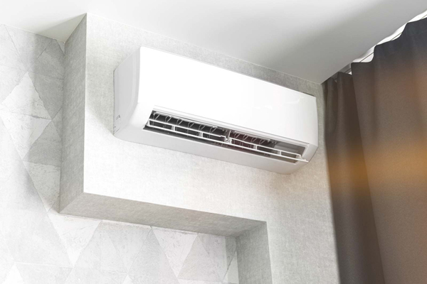 A white wall-mounted air conditioning unit, ideal for efficient cooling and easy mini-split repair, is installed near the ceiling in a modern room with a geometric patterned wall and a dark curtain.